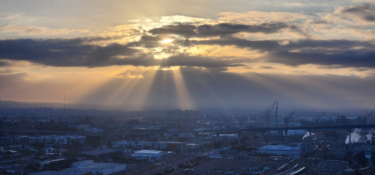 Sunbeams breaking through clouds over a wide city view