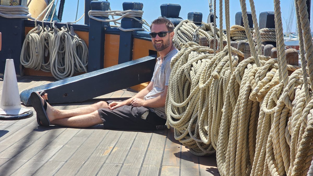 A man sitting on the deck of a historic tall ship among coiled ropes