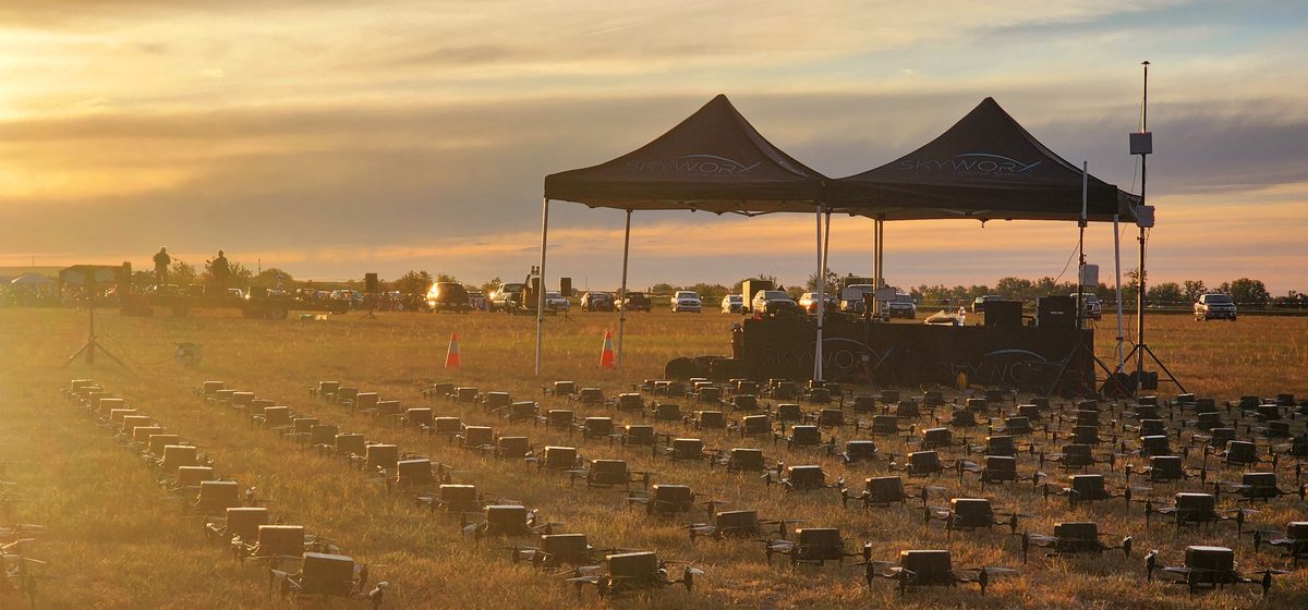 Pop-up tents above rows of drones in a field at golden hour