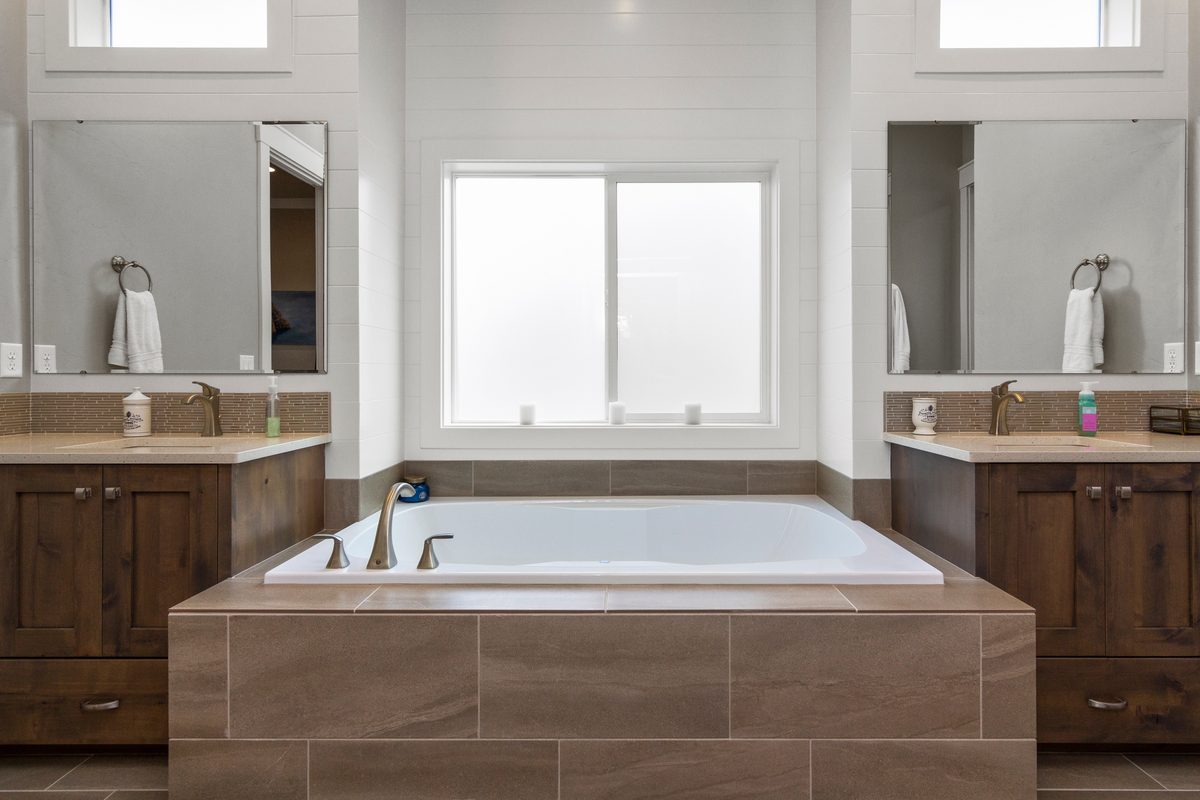 Bathroom with a tiled soaking tub surround between two wood vanities