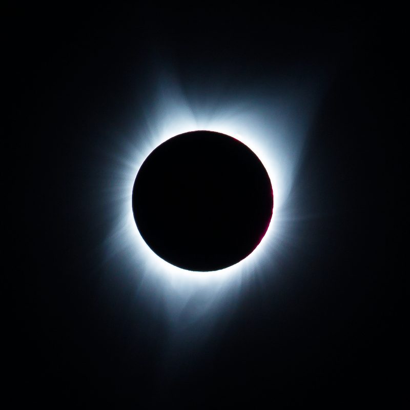 The white corona glows around the black moon during totality of a solar eclipse.
