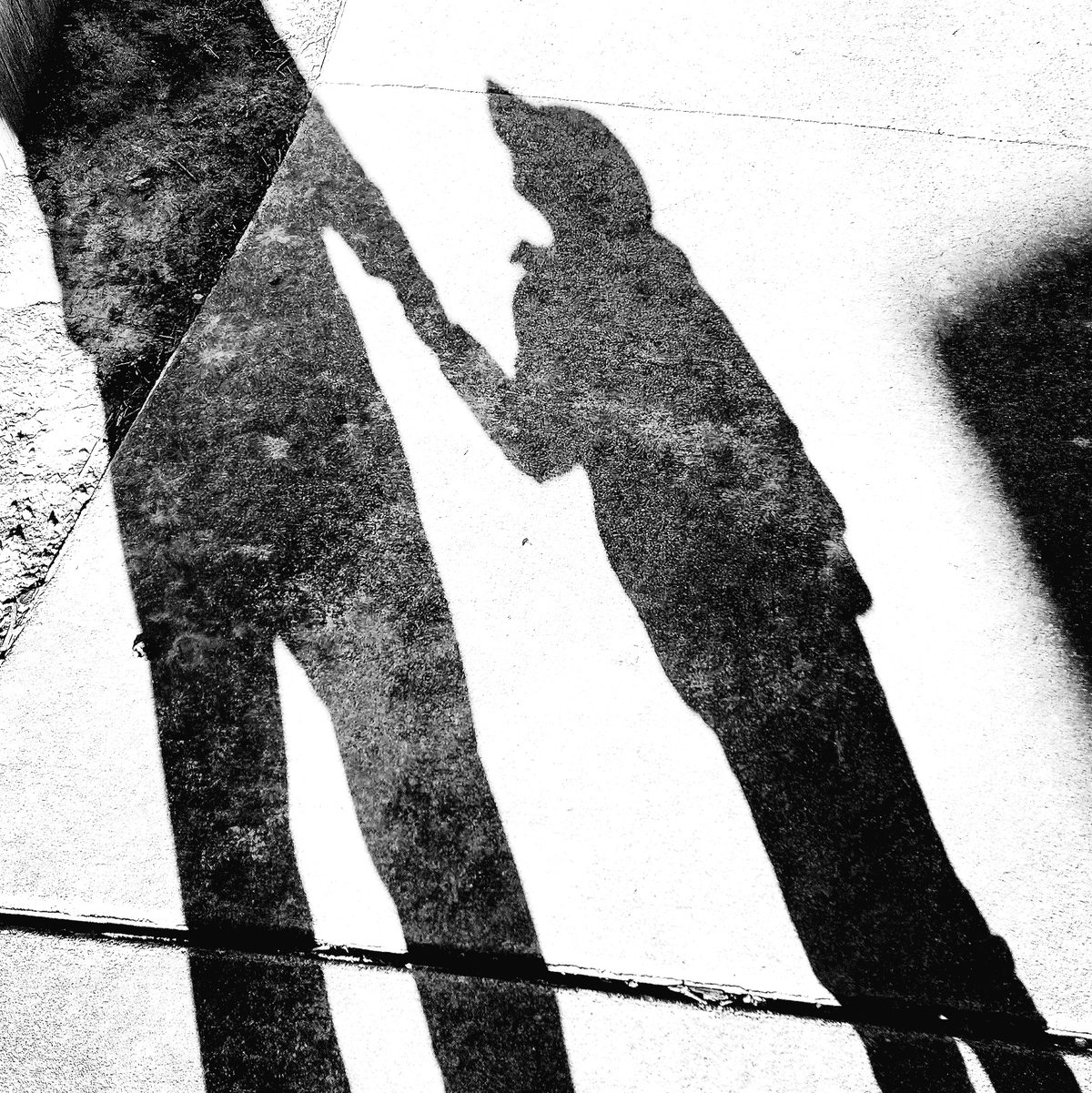 High-contrast black-and-white shadows of two people stretched across the pavement