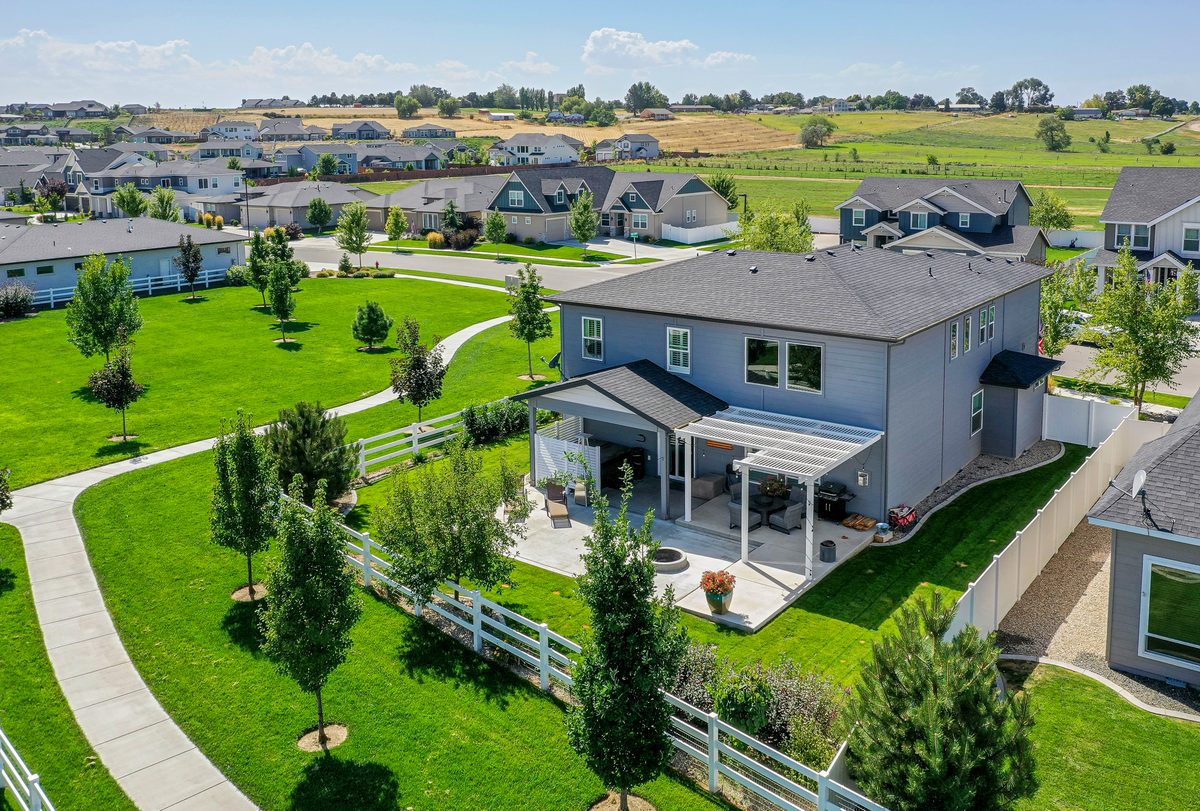 Drone photo of a two-story home with a white-fenced yard in a green subdivision
