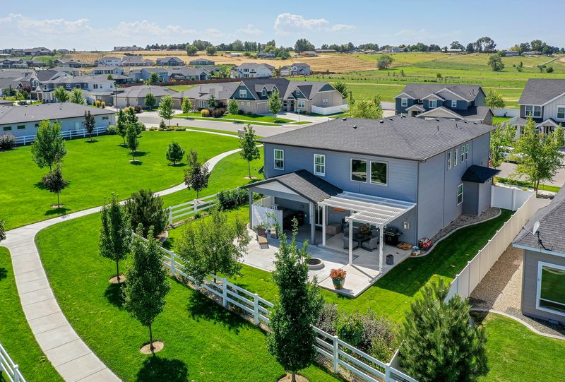 Drone photo of a two-story home with a white-fenced yard in a green subdivision