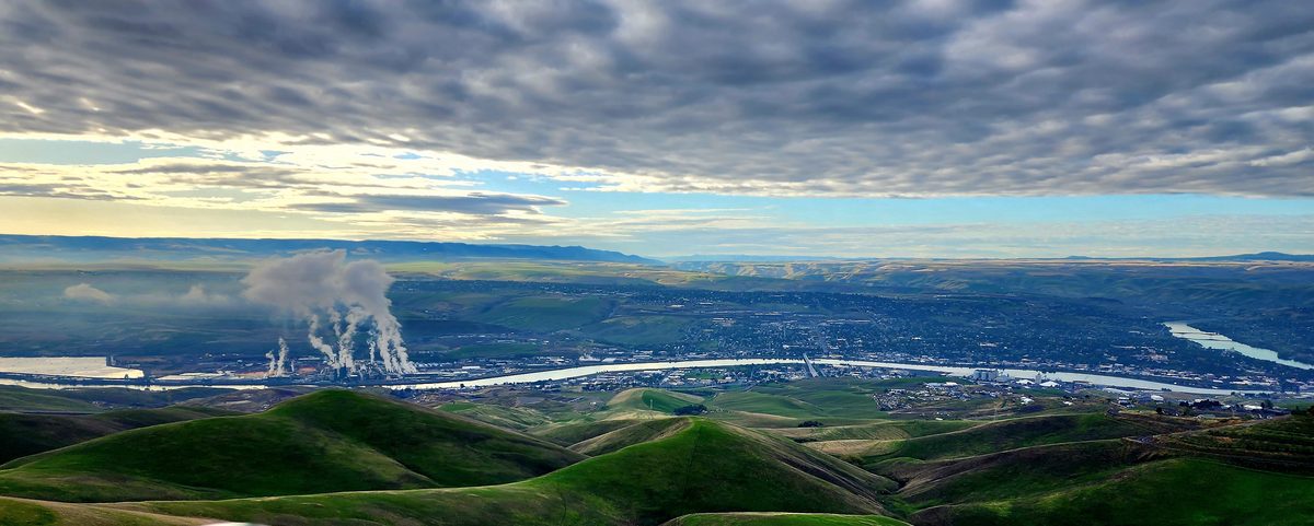 A green valley with distant steam plumes under a broad morning sky