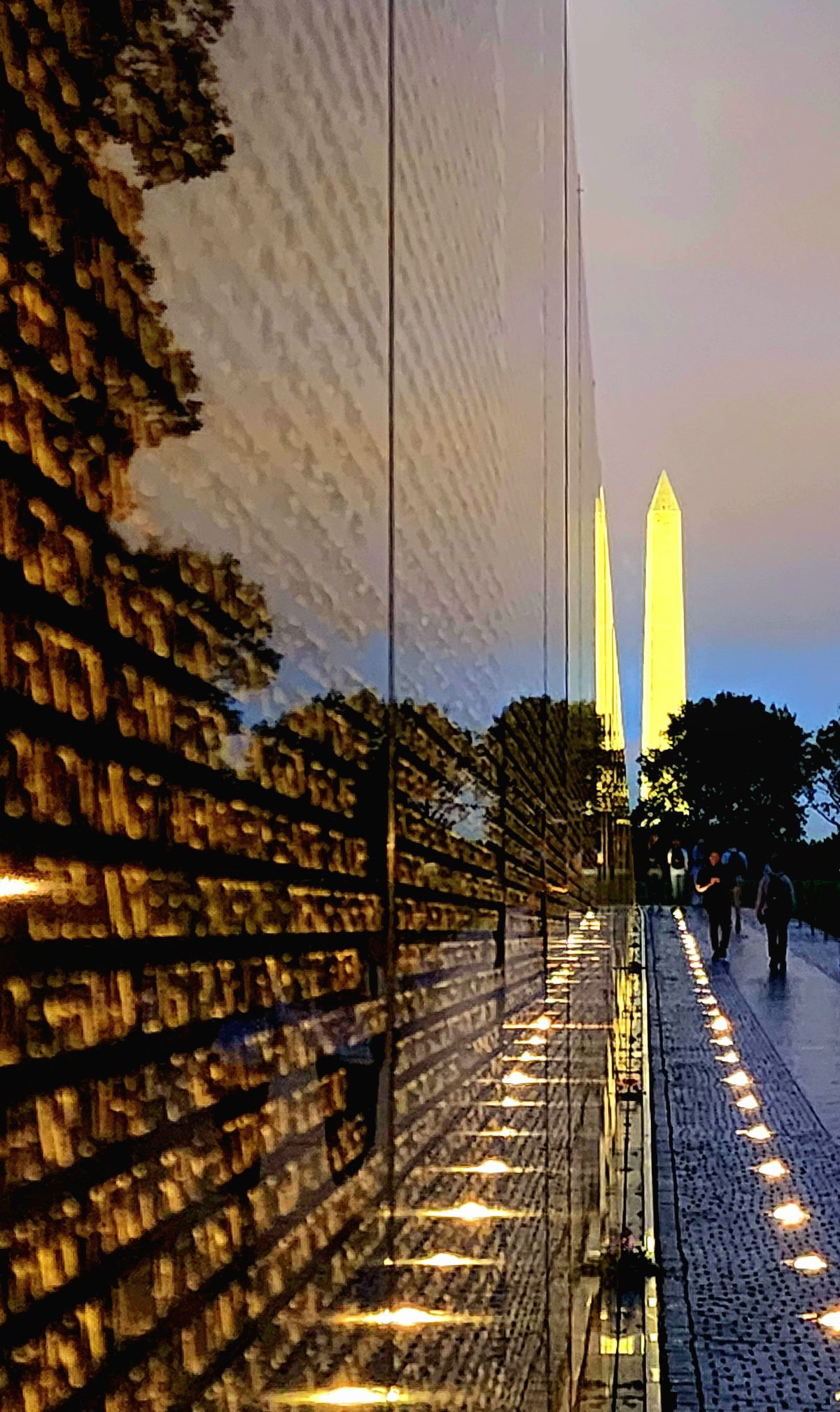 The Washington Monument framed by the lit stone wall of a memorial at dusk