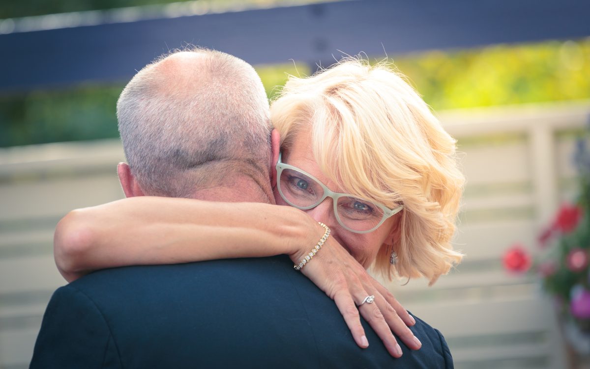 A bride wrapping her arms around the groom's neck in a warm outdoor embrace
