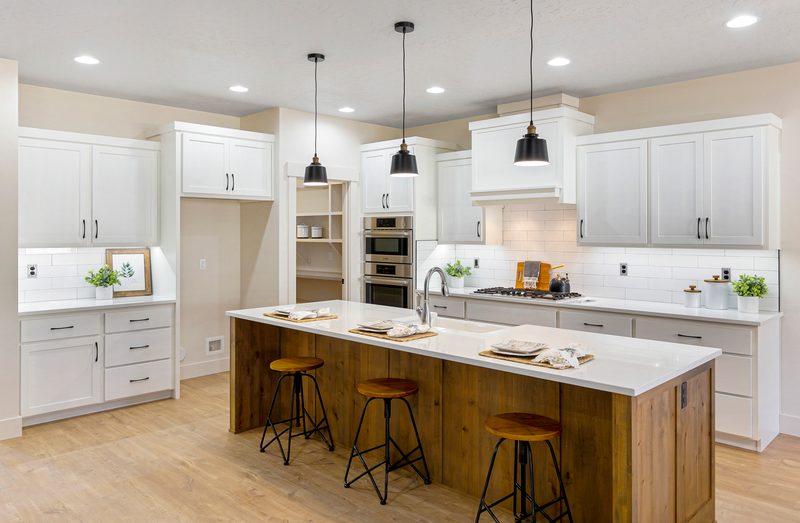 White kitchen with three pendant lights over a natural wood island and bar stools