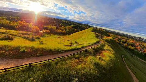 FPV drone flies over grassy hills and dirt trails as the sun sets behind them, autumn trees beyond