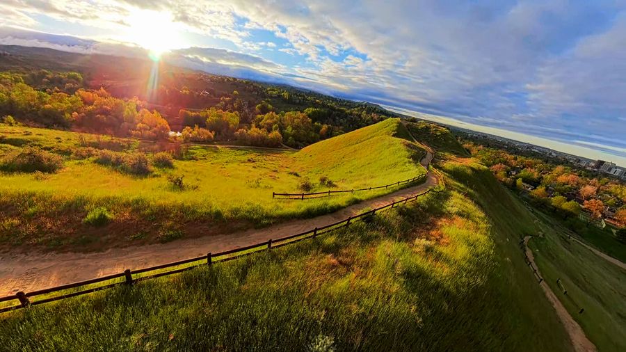 FPV drone flies over grassy hills and dirt trails as the sun sets behind them, autumn trees beyond