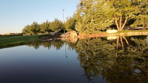 FPV drone weaves low through office-campus gardens, past a pond, flower beds and stone walls in golden light