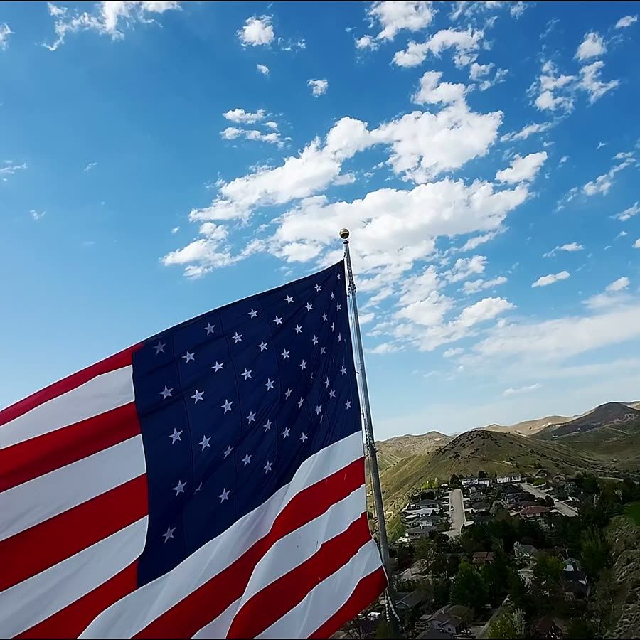 FPV dive past a huge US flag above a hillside neighborhood
