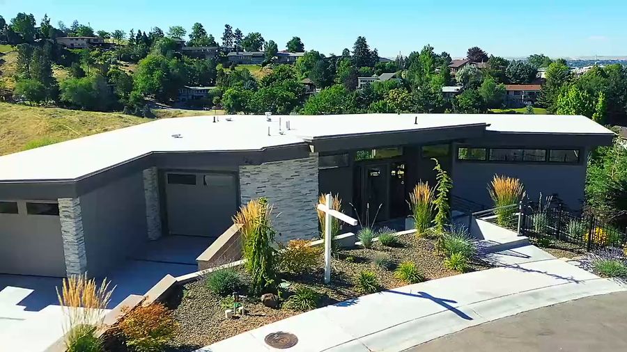 Drone orbits a modern three-story home on a hillside above the city