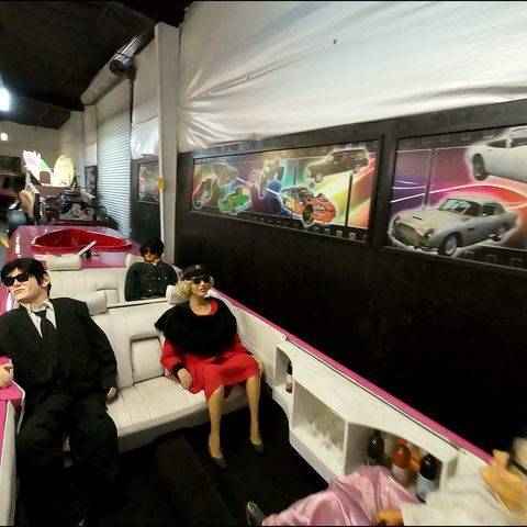 FPV drone flies low through a museum of movie and TV cars, past a Batmobile and a cartoon Taz car