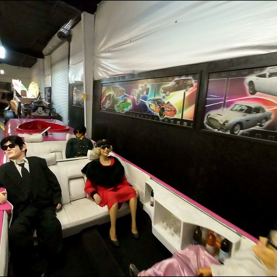 FPV drone flies low through a museum of movie and TV cars, past a Batmobile and a cartoon Taz car