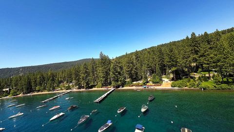 Drone rises from a pine shoreline over a clear turquoise bay full of anchored boats on Lake Tahoe