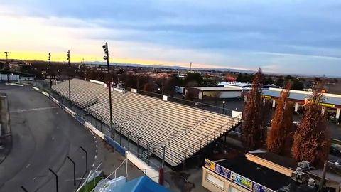 Drone swoops around an empty oval race track and grandstand at sunset, the Meridian water tower behind it