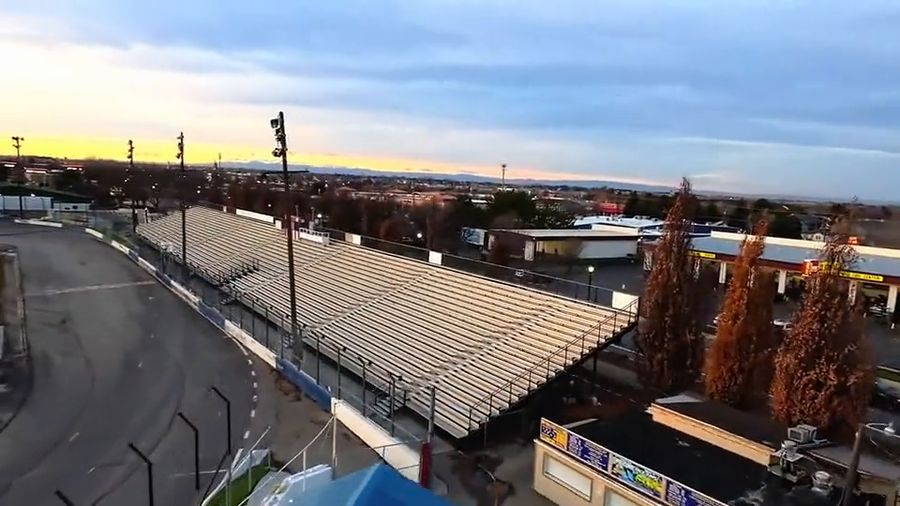 Drone swoops around an empty oval race track and grandstand at sunset, the Meridian water tower behind it