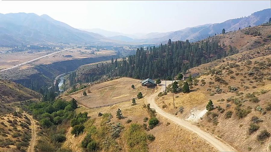 Drone flight over a ranch home and shop on a foothill above a forested canyon