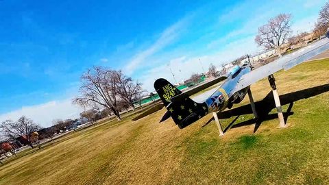 FPV drone dives from the lake view to fighter jets on display in a city park, then follows a wetland trail