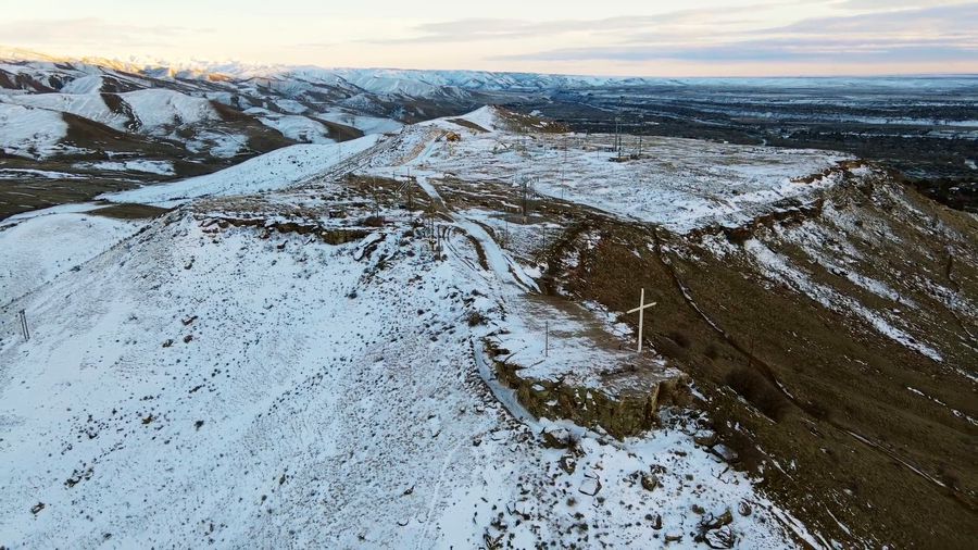 Drone climbs over Table Rock's snowy foothills above Boise as the sun breaks through over the city