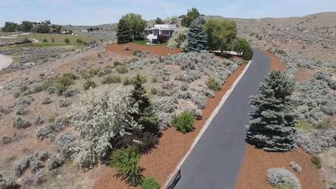 Drone flies up a winding drive to a white stucco estate on a sagebrush hill